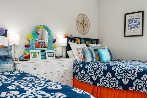 A bedroom with two beds, a dresser, a mirror, and various decorative items. - CAMP QUEENIE - 2nd row with great views, steps to the surf and sand! (Crystal Beach)