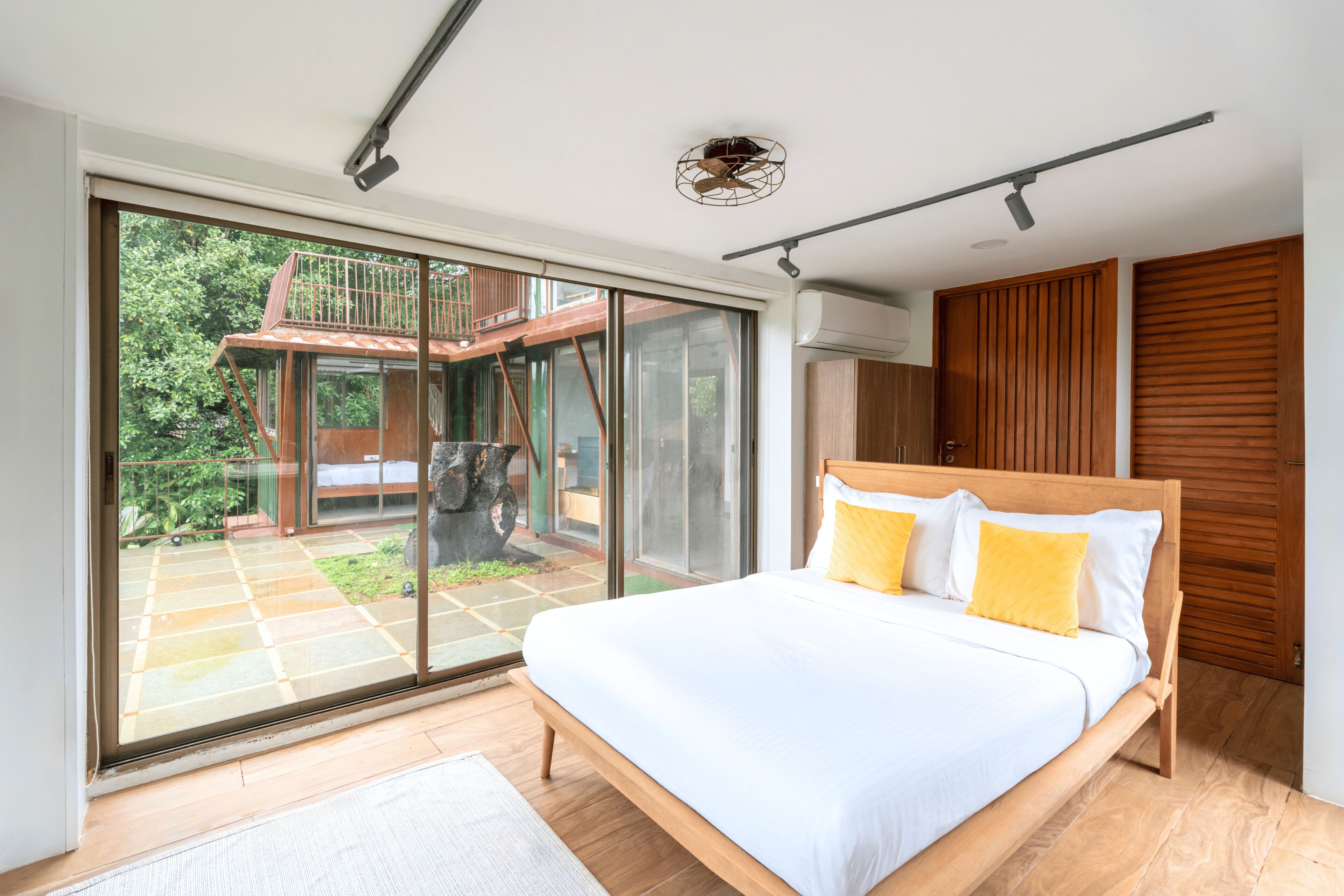 A modern bedroom with a large bed, sliding glass doors leading to an outdoor area, and a wooden ceiling structure.