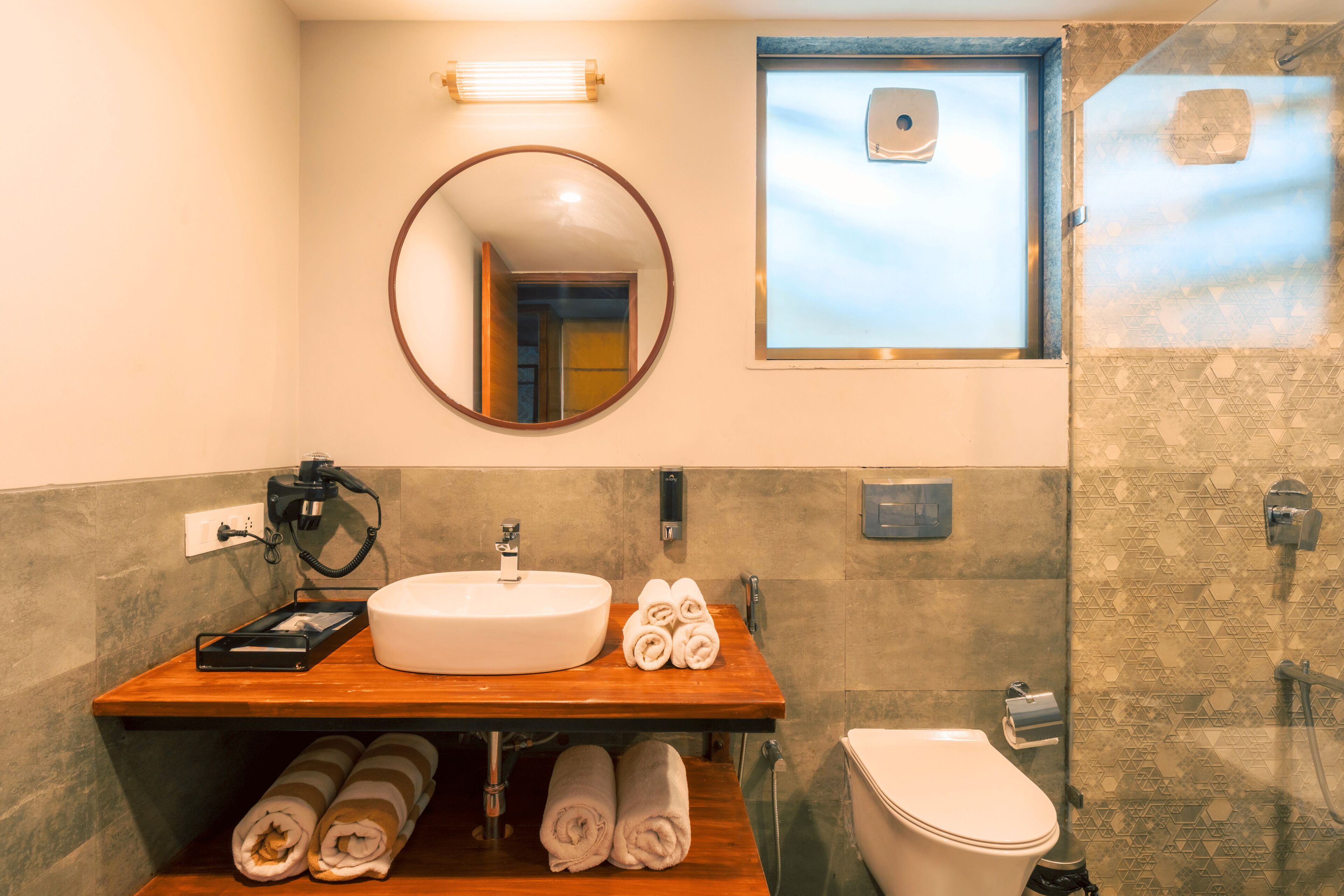 A bathroom with a wooden vanity, a round mirror, a sink, and a toilet.