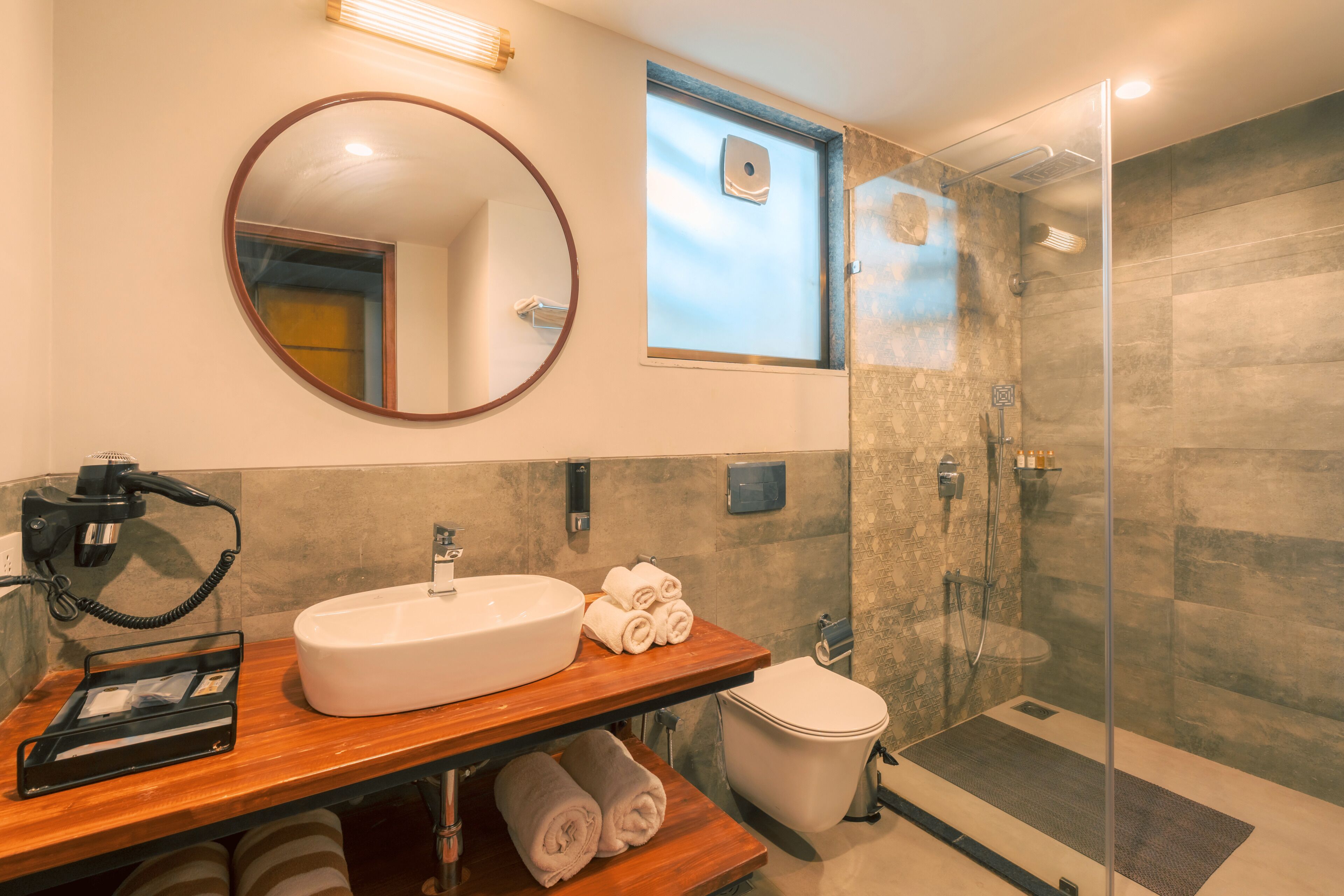 Un baño moderno con un espejo redondo, un lavabo, un inodoro y una ducha con mampara de vidrio.