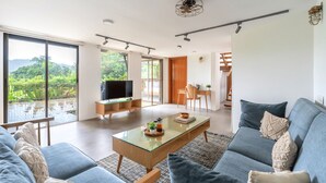 En rummelig stue med et sofabord i glas, en blå sofa og udsigt til grønne omgivelser.