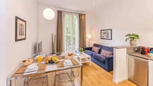 A modern living space with a dining area, a sofa, and a kitchen area.