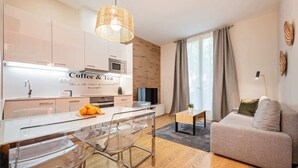 Ett modernt kök med en central köksö, en matplats med genomskinliga stolar, en soffa och en tv.