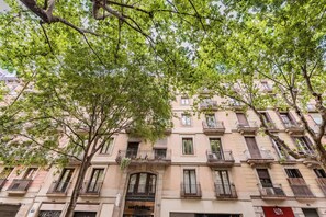 A multi-story building with balconies, a ground-floor entrance, and a tree in the foreground. - Sweett | Villarroel 311 (Barcelona)