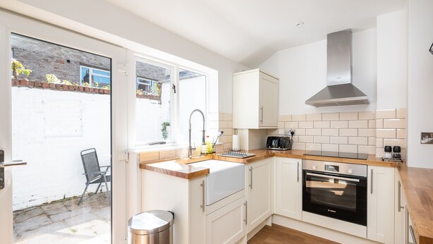Une cuisine moderne avec des meubles blancs, un four Bosch, une hotte de cuisson en acier inoxydable et une fenêtre donnant sur un jardin.