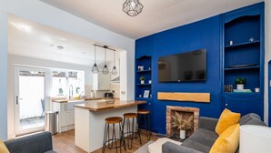 Un salon moderne avec un canapé gris, des coussins jaunes, une cheminée et un téléviseur fixé à un mur bleu.