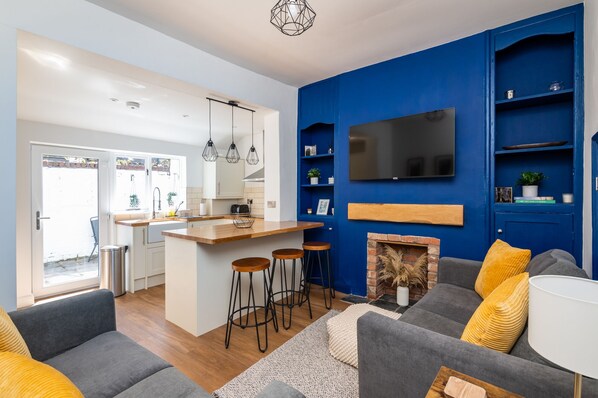 A modern living room with a grey sofa, yellow cushions, a fireplace, and a TV mounted on a blue wall.