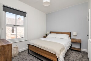 A bedroom with a bed, bedside tables, a nightstand, a lamp, and a window with a view of buildings.