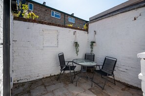 A small outdoor patio with a round table and four chairs, surrounded by white brick walls and a stone floor.