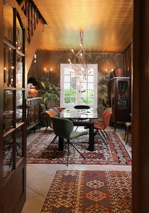 Zona pranzo con tavolo in legno, sedie, un lampadario e un tappeto decorato.