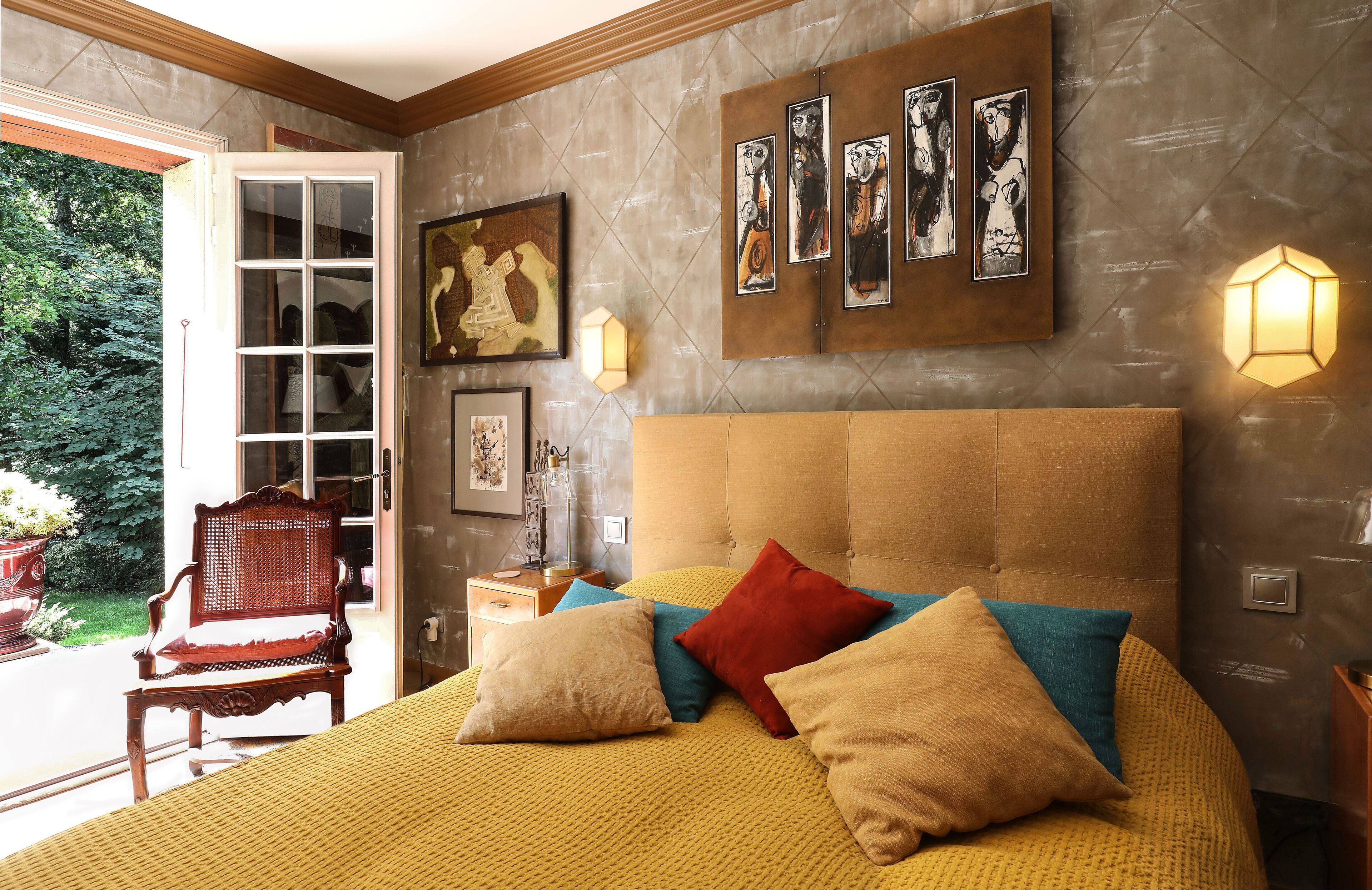 Une chambre avec un grand lit, de nombreux oreillers, un banc en bois et des œuvres d’art accrochées au mur.