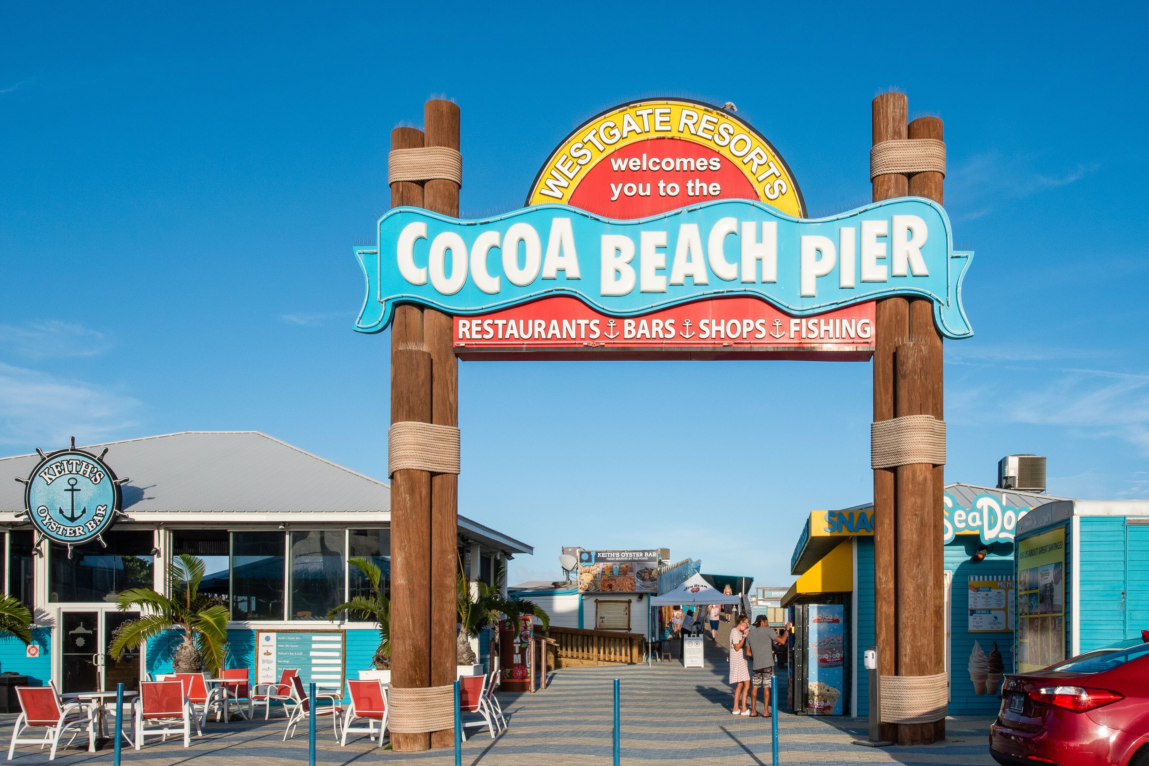 A sign for Cocoa Beach Pier with a welcoming message, a seafood restaurant, and a bar.