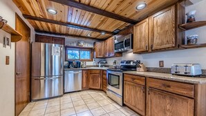 Una cocina con armarios de madera, electrodomésticos de acero inoxidable y piso de baldosas.