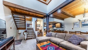 Un salón amplio con un sofá grande, una mesa de centro de madera y una escalera que conduce a un nivel superior.