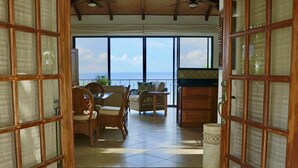 A room with a view of the ocean, a dining area with wicker furniture, and a wooden cabinet.
