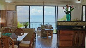 A spacious living area with a view of the sea, a dining set, and a kitchen area.