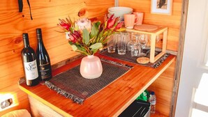 En interiör med träinredning och en bardisk med två vinflaskor, en vas med blommor och en hög med tallrikar och glas.