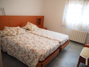 Una cama doble con ropa de cama floral, un cabecero de madera, un estante pequeño y un radiador.