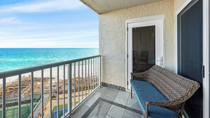 Un balcon avec un canapé en osier, une porte et une vue sur la plage et l’océan.