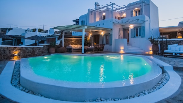 A modern villa with a swimming pool, outdoor seating, and a stone wall. -  6Bedroom Villa with private pool, located in Kalafatis, Mykonos (Καλαφάτη, Μύκονος)