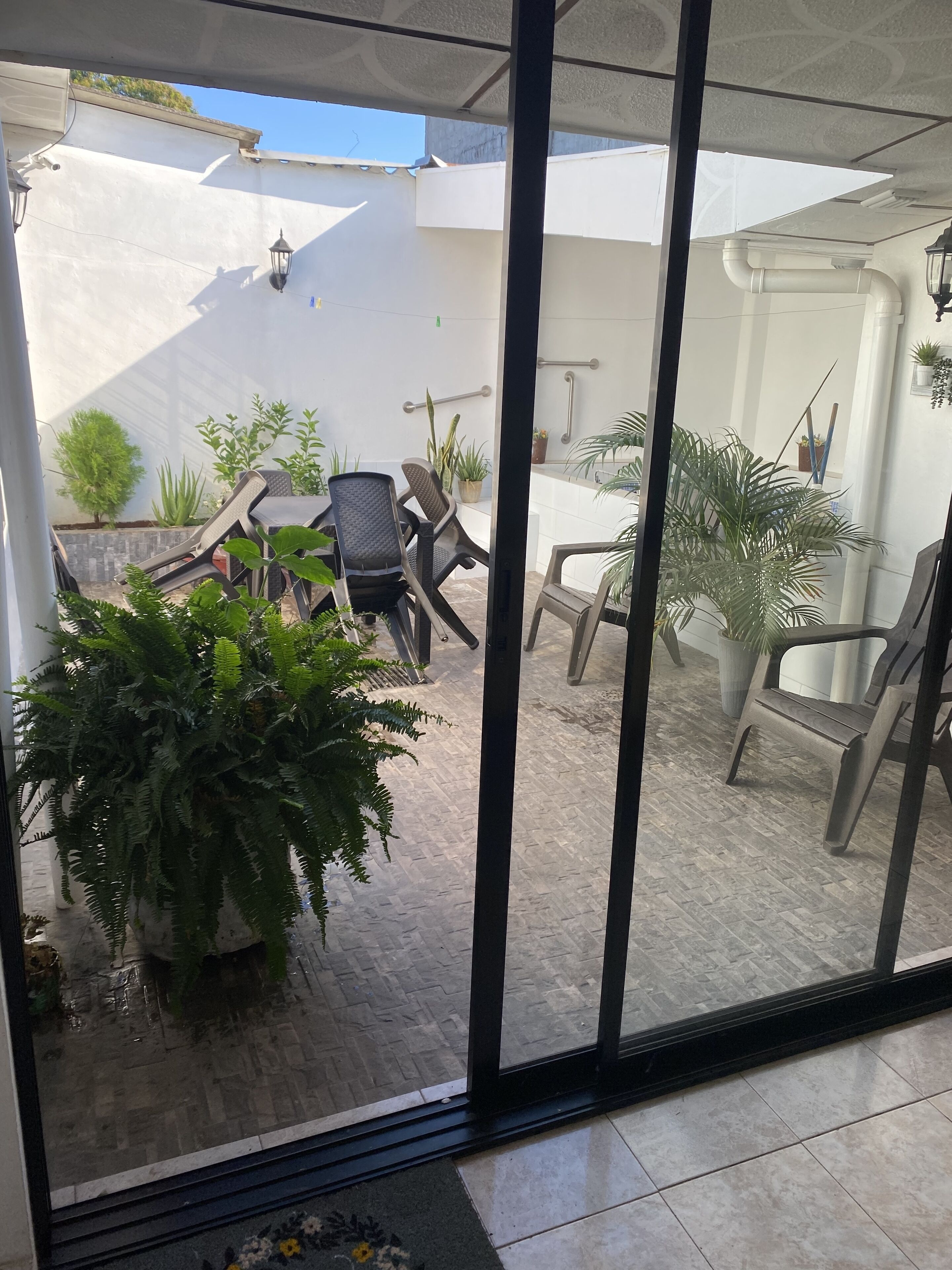 A covered outdoor patio with a table and chairs, surrounded by potted plants and a small garden area.