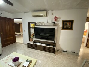 A living room with a flat-screen TV, a wooden cabinet below, and a small shelf with decorative items. - Beautiful house to relax, very close to shops and restaurant (Sonzacate)