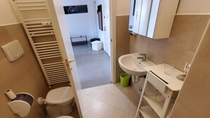 A compact bathroom with a toilet, sink, and bathtub. A towel rack and a green trash bin are visible. - Residence Bonomelli apt. no. 18 two-room apartment (Bergamo)