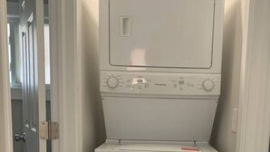 A compact, white laundry machine in a narrow hallway with a door on one side and a wall on the other. - Modern and Chic in German & Merion Village Area (Columbus)