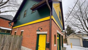 A two-story house with a green and yellow facade, a yellow front door, and a brick exterior. - Cozy and Modern Short North Carriage House (Columbus)