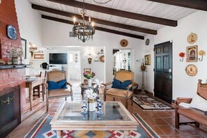 Un salon avec un lustre, deux fauteuils, une table basse et une cheminée.