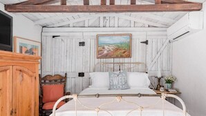 A bedroom with a bed, a wooden wardrobe, a chair, a painting on the wall, and a nightstand with a lamp and flowers. - 3BR w/ Pool + Outdoor Fireplace | Near Downtown (Palm Springs)