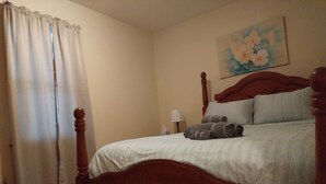Ein Schlafzimmer mit einem hölzernen Himmelbett, einer weiß gestreiften Bettdecke und gerollten Handtüchern auf dem Bett. An der Wand hängt ein Blumenbild und auf einem Nachttisch steht eine Lampe.