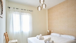 A hotel room with a bed, a chair, a window with curtains, and a wall-mounted light fixture.