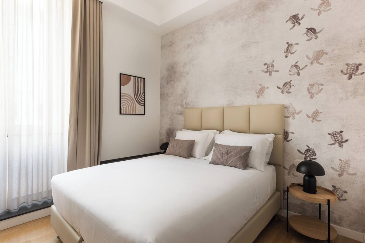 A modern bedroom with a large bed, a headboard, and a wall with a turtle pattern.