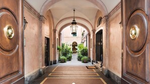 Un pasillo con techos abovedados y puertas de madera, que conduce a una zona central con plantas y una lámpara colgante.