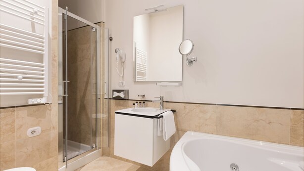 Un baño moderno con cabina de ducha de vidrio, un lavabo blanco con una toalla, un espejo grande y una bañera.