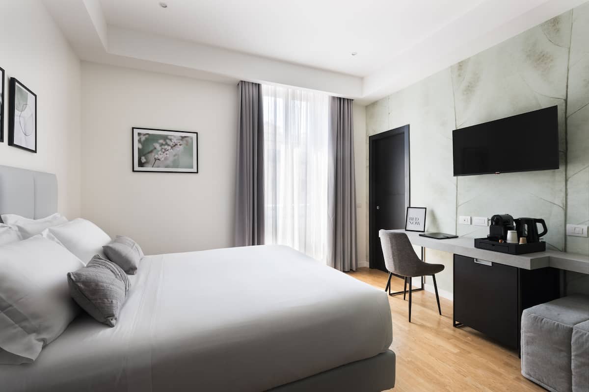 A modern hotel room with a large bed, a desk, a chair, and a television.