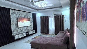 A living room with a flat-screen TV, a ceiling fan, a sofa, and a patterned rug.