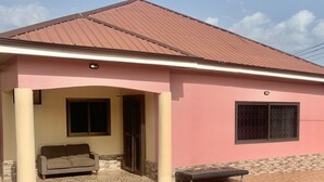 A building with a pink exterior, a tiled patio, a sofa, and a bench.