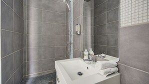 Ein modernes Badezimmer mit einer großen Dusche, einem Waschbecken mit Spiegel und einem Handtuchhalter.