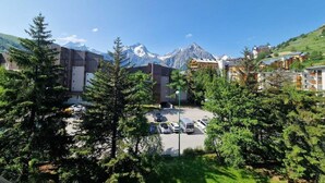 A hotel with a parking lot, surrounded by trees and mountains in the background. - 50m from resort center, 4th floor, view mountain, balcony, parking, tv, ski locker, 30m² (Les Deux Alpes)