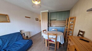A compact living space with a blue sofa, a dining table with chairs, a wooden dresser, and a kitchenette in the background. - 50m from resort center, 4th floor, view mountain, balcony, parking, tv, ski locker, 30m² (Les Deux Alpes)