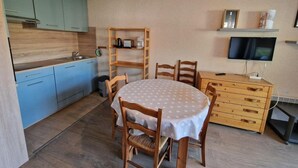 A compact kitchen with a dining area, wooden cabinets, a TV, and a small shelf. - 50m from resort center, 4th floor, view mountain, balcony, parking, tv, ski locker, 30m² (Les Deux Alpes)