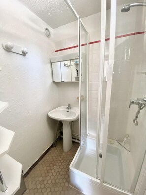 A bathroom with a glass-enclosed shower, a pedestal sink, and a mirror above the sink.