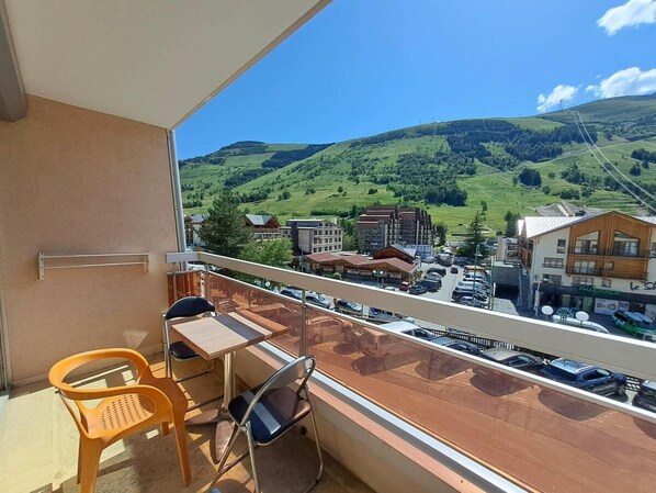 A balcony with a view of a town and hills, a table, two chairs, and a railing.
