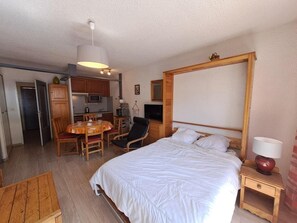A bedroom with a bed, bedside table, lamp, and a dining area with chairs and a table.