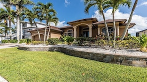 A two-story house with a stone retaining wall, palm trees, and a well-maintained lawn.