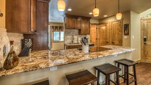 Una cocina con gabinetes de madera, encimeras de granito e iluminación colgante.