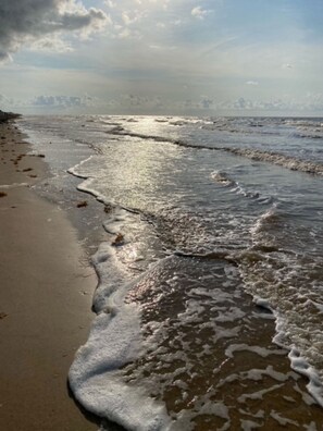 A beach with waves lapping onto the shore, a clear sky, and distant land. - Sargent Beach Getaway - Have Fun in the Sun! (Sargent)