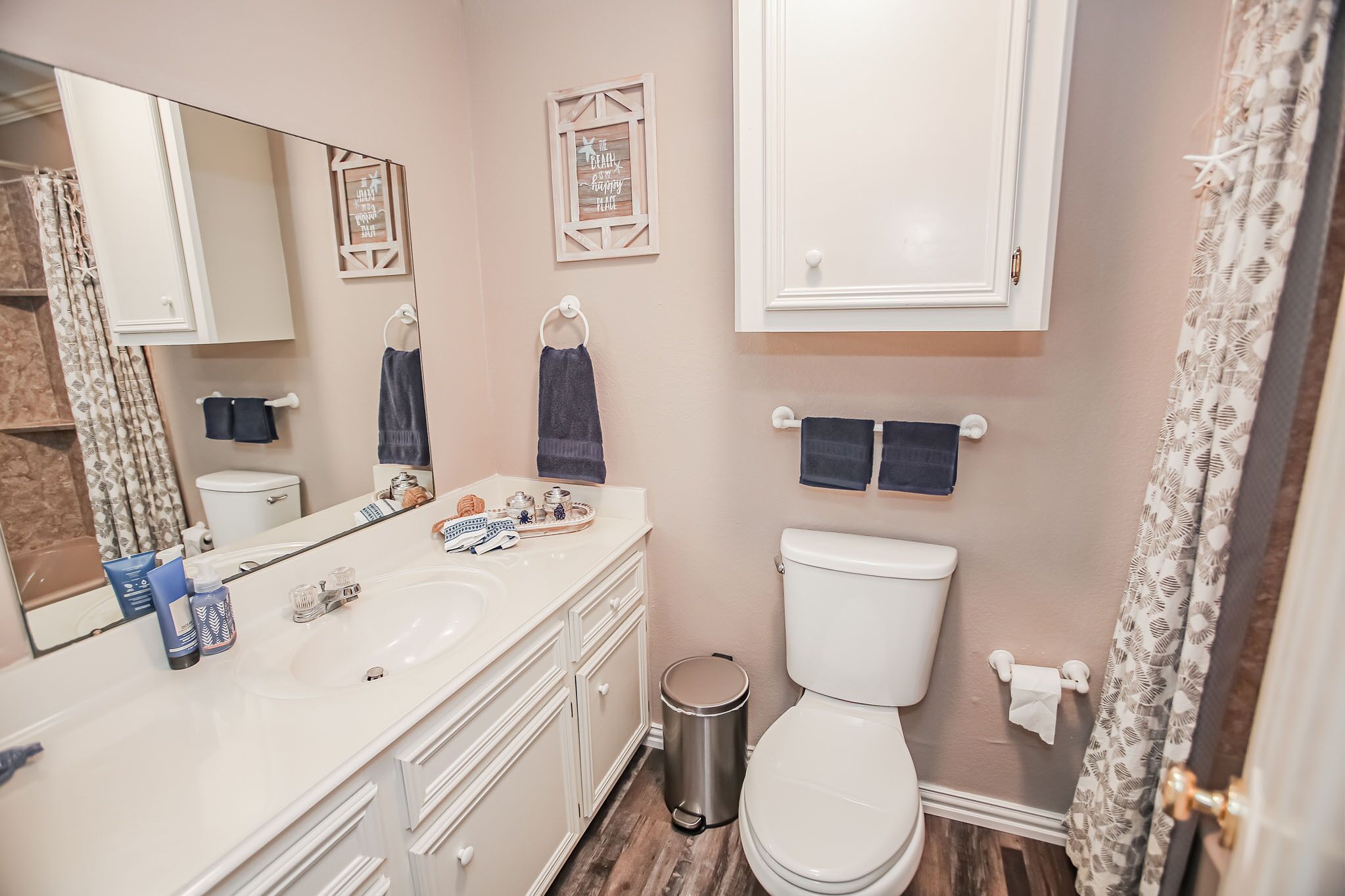 A bathroom with a white sink, two towel racks, a toilet, and a trash can.